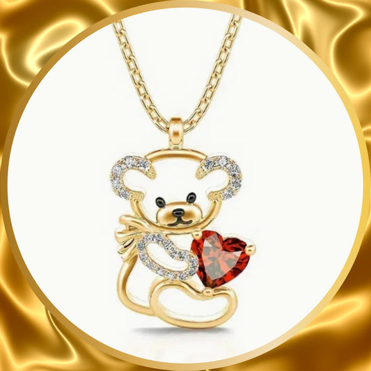 A cutest little bear with crystal stones ears and arm holding a red heart stone gold plated necklace.